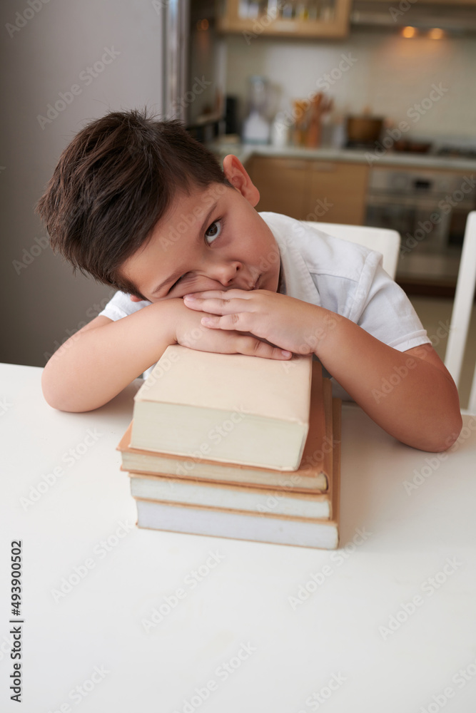 Tired and bored little boy leaning on stack or school books and looking at camera Tired and bored little boy leaning on stack or school books and looking at camera