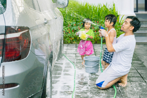 Two little kids help their father to washing a car