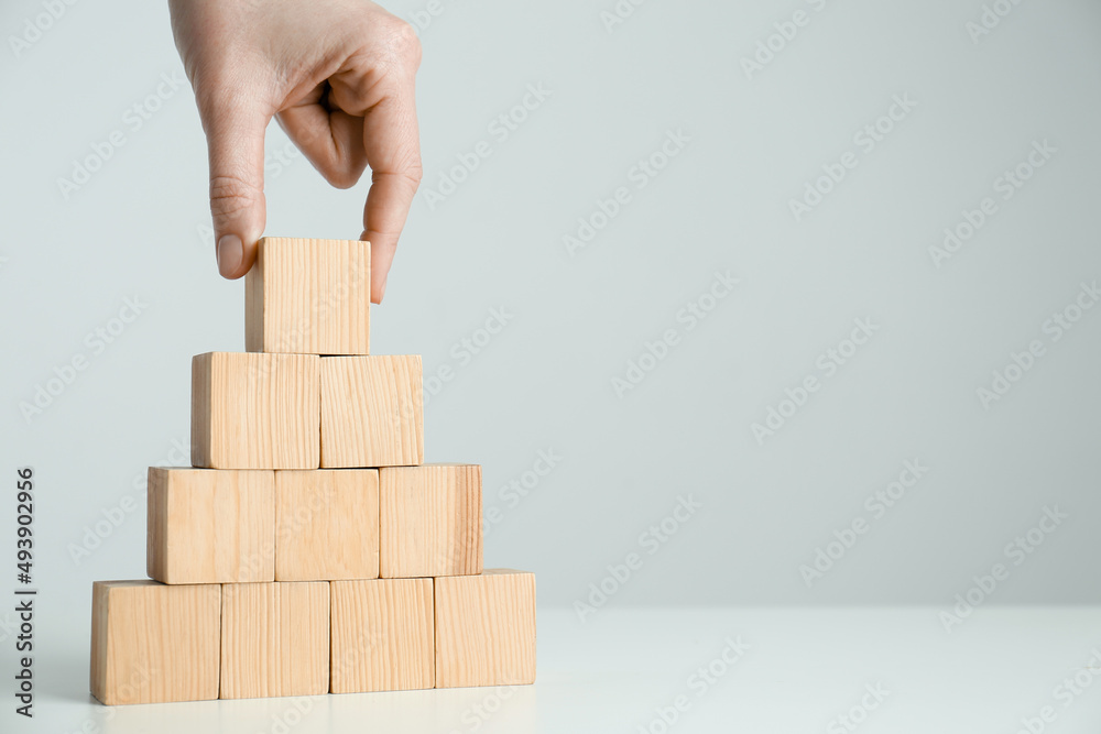 Woman building pyramid of blank wooden cubes on white table against light background, closeup. Space for text Woman building pyramid of blank wooden cubes on white table against light background, closeup. Space for text