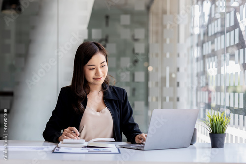 A beautiful Asian businesswoman sitting in her private office, she is checking company financial documents, she is a female executive of a startup company. Concept of financial management.