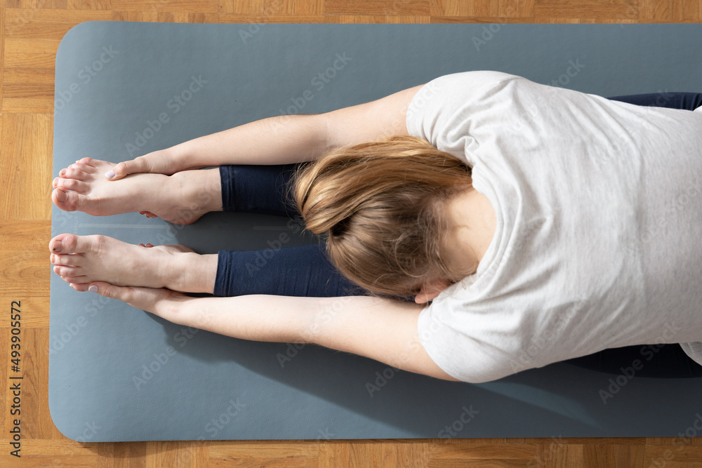 View from above of woman stretching hamstring muscles holding her feet with hands. View from above of woman stretching hamstring muscles holding her feet with hands.