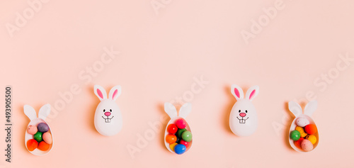 Top view festive Easter beige peach color background with funny bunny eggs containers filled with candy chocolate eggs. Bunny rabbit symbol. Easter egg hunt. Creative Easter wide banner. Copy space.