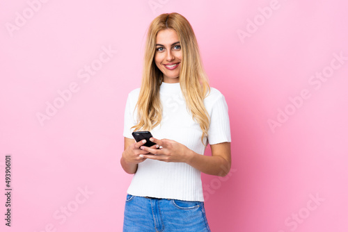 Young Uruguayan blonde woman over isolated pink background sending a message with the mobile