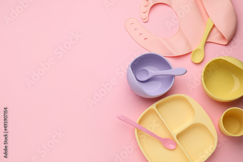 Flat lay composition with baby feeding accessories and bib on pink background, space for text