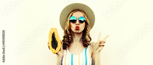 Summer portrait of beautiful young woman model posing with papaya wearing straw hat, sunglasses on white background