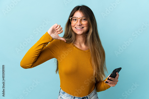 Young caucasian woman using mobile phone isolated on blue background proud and self-satisfied