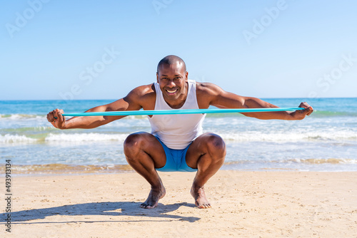 Smiling sportsperson with resistance band crouching at beach photo