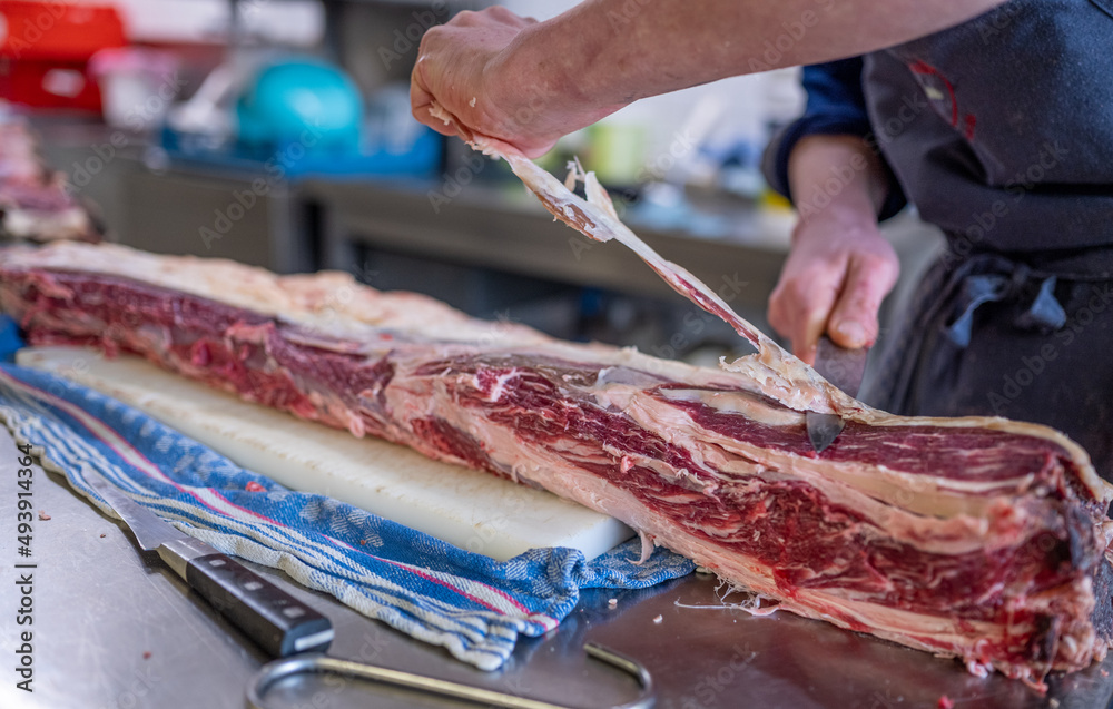 Großes Dry Aged Rippe Steak wird von einem Koch in der Küche mit einem Messer zerlegt und bearbeitet 