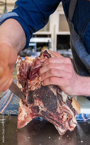 Großes Dry Aged Rippe Steak wird von einem Koch in der Küche mit einem Messer zerlegt und bearbeitet  photo