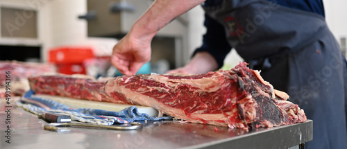 Großes Dry Aged Rippe Steak wird von einem Koch in der Küche mit einem Messer zerlegt und bearbeitet 