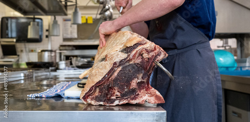 Großes Dry Aged Rippe Steak wird von einem Koch in der Küche mit einem Messer zerlegt und bearbeitet  photo