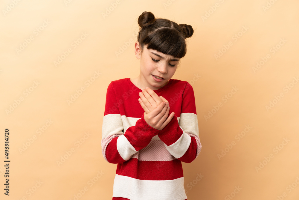Little caucasian girl isolated on beige background suffering from pain in hands Little caucasian girl isolated on beige background suffering from pain in hands
