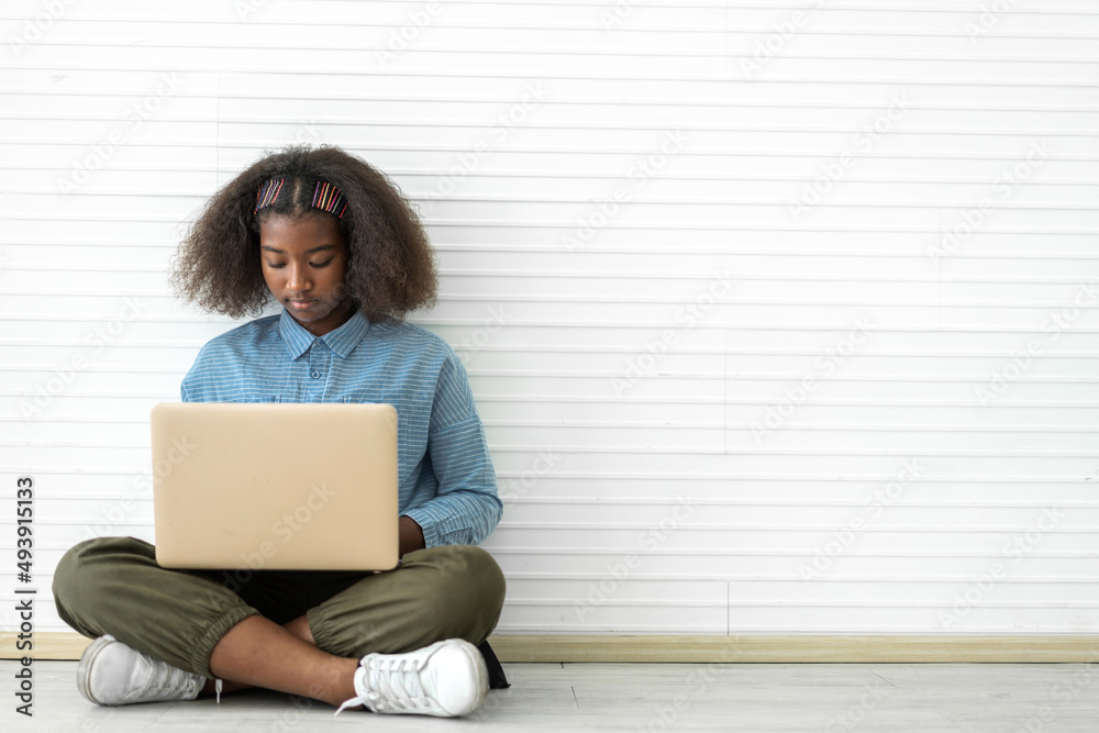 Fototapeta premium Portrait of smile black african american cute student little girl child sitting on floor using technology laptop computer typing on keyboard learn and study on white wall background