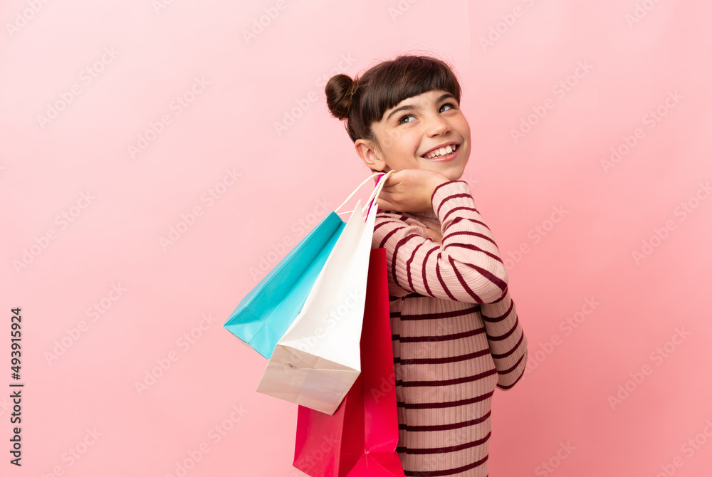 Little caucasian girl isolated on pink background holding shopping bags and smiling Little caucasian girl isolated on pink background holding shopping bags and smiling