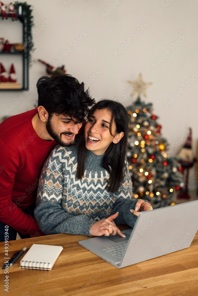 Happy man embracing girlfriend sitting with laptop at home Happy man embracing girlfriend sitting with laptop at home
