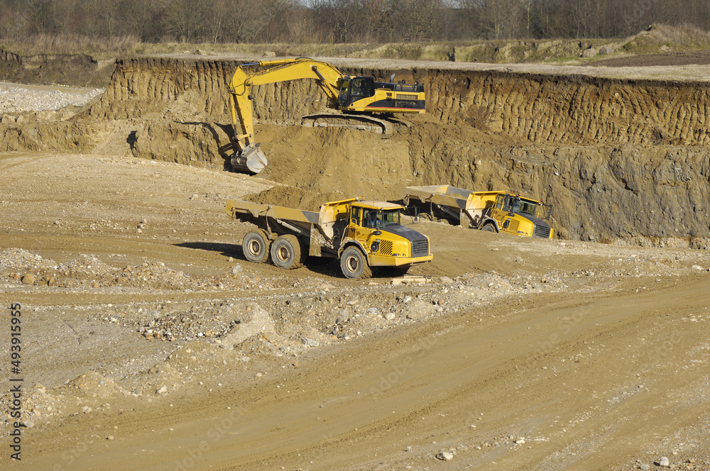 Yellow dump trucks and excavator are working in gravel pit