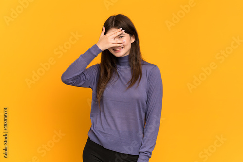 Young Ukrainian girl isolated on yellow background covering eyes by hands and smiling © luismolinero