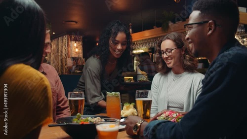 Diverse group of friends eating at restaurant while female waitress delivers food