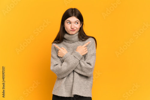 Young Ukrainian girl isolated on yellow background pointing to the laterals having doubts © luismolinero