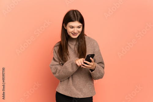 Young Ukrainian girl isolated on pink background sending a message or email with the mobile