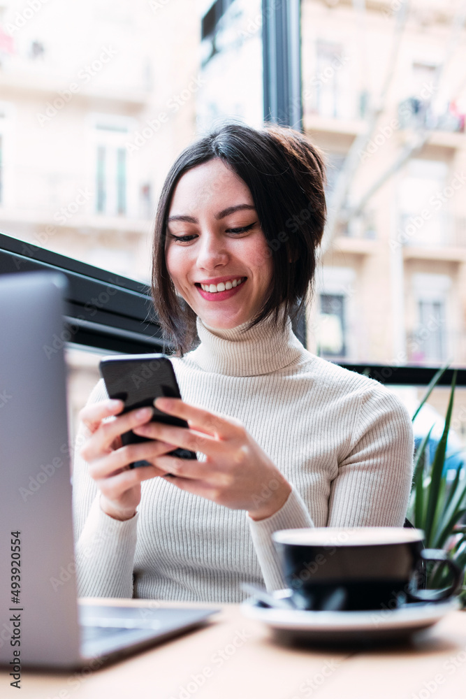 Happy businesswoman with laptop using mobile phone sitting at cafe Happy businesswoman with laptop using mobile phone sitting at cafe