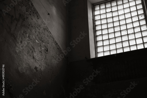 Entrance with large panoramic window of an abandoned old building, cracked paint on wall inside room. Monochrome, black and white photography