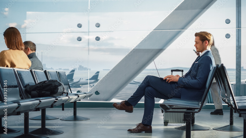 Airport Terminal: Businessman Uses Laptop Computer, Waiting for Flight to International Conference. Traveling Entrepreneur Remote Work Online Sitting in a Boarding Lounge of Airline Hub with Airplanes