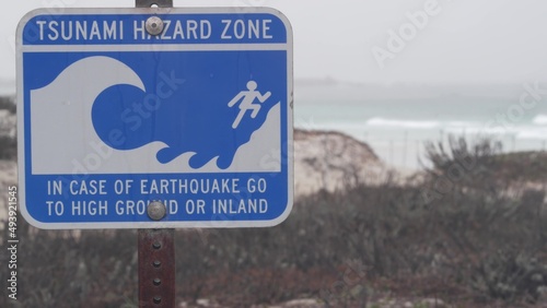 Ocean beach sandy dunes, Monterey, California misty coast, USA. Foggy rainy autumn, winter weather, grey cloudy sky. Trail path on shore, cold sea waves. Warning sign, tsunami hazard. Danger caution.