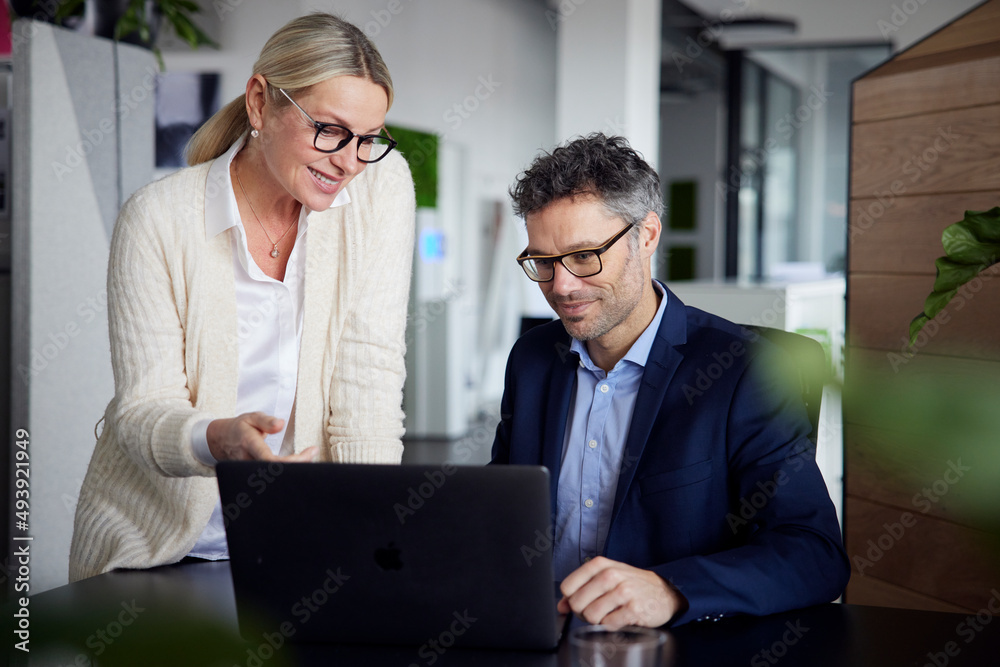 Smiling businesswoman discussing with colleague over laptop at desk in office Smiling businesswoman discussing with colleague over laptop at desk in office