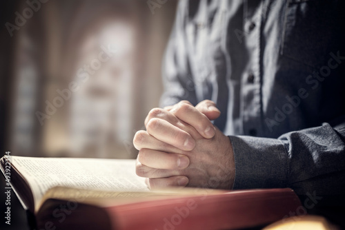 Hands folded in prayer on a Holy Bible in church, faith, spirtuality and religion