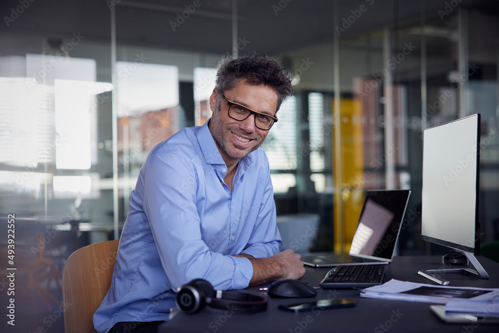 Happy businessman wearing eyeglasses sitting at desk in office Happy businessman wearing eyeglasses sitting at desk in office