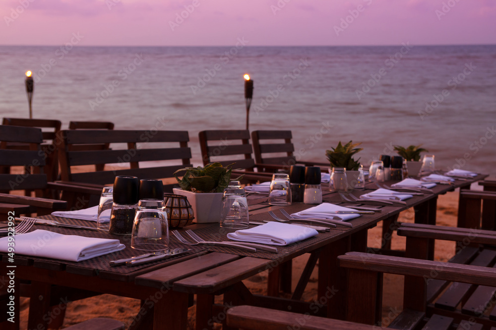 Outdoor restaurant table dinner setting on beach at sunset