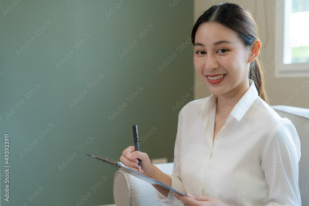 Asian businesswoman smiling and holding a clipboard in office. Beautiful and good looking Asian woman sits on the sofa. female portraits. Asian businesswoman smiling and holding a clipboard in office. Beautiful and good looking Asian woman sits on the sofa. female portraits.
