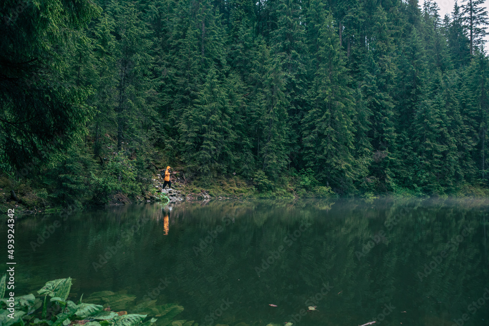 woman hiker in yellow raincoat at lake beach