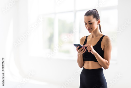Attractive healthy young woman with a fitness mat using mobile phone at the gym