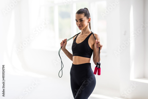 Portrait of muscular young woman exercising with jumping rope on white background.