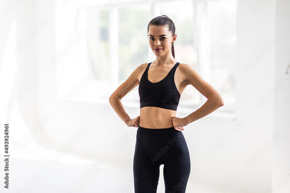 Portrait of beautiful fitness woman smiling and looking at camera isolated on grey background. Young woman in sportswear relaxing after training at gym.
