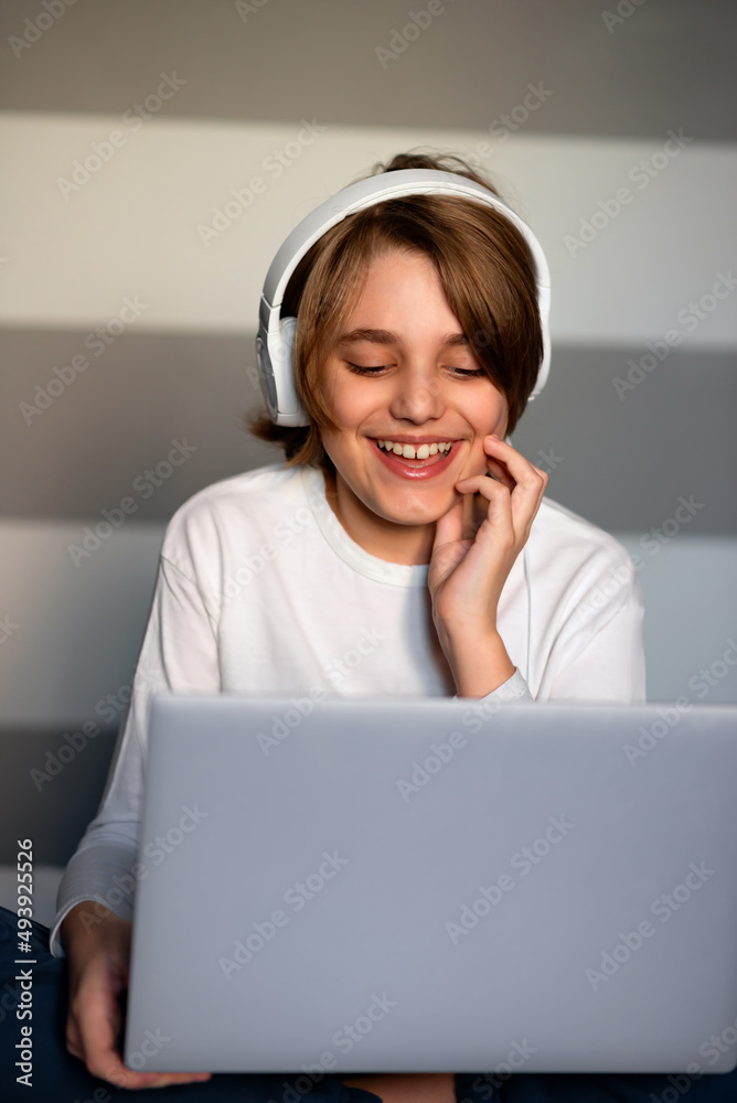 Happy teenager boy looking at laptop screen and laughing. Boy having lessons, studying online at home, communicating. Distance education concept. Home interior. Happy teenager boy looking at laptop screen and laughing. Boy having lessons, studying online at home, communicating. Distance education concept. Home interior.