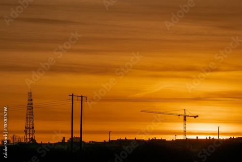 Sunset of sunrise scene. Silhouette of a tall crane against warm orange color sky. Urban construction background. Calm mood.