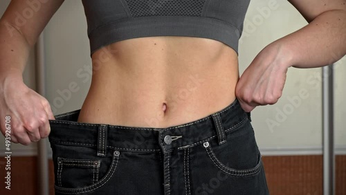 Girl with a beautiful figure tries on old big jeans and checks the result. Woman after diet and sport with beautiful waist. Slim figure after weight loss.