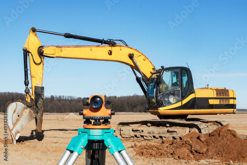 Level with an excavator in the background. Construction level or theodolite. Geodetic instruments and equipment for the construction and earthworks.