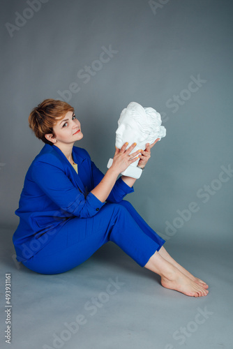 Elegant woman in a blue classic suit on a gray background. Plaster model of a woman's head. Plaster head