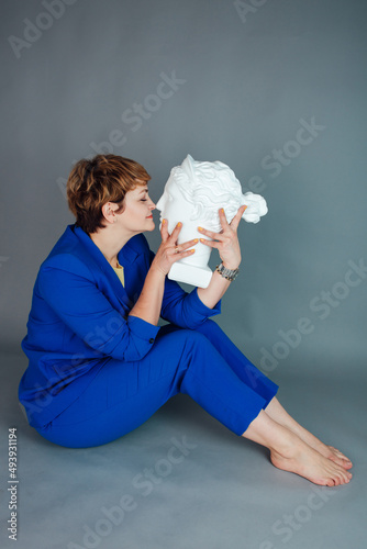 Elegant woman in a blue classic suit on a gray background. Plaster model of a woman's head. Plaster head