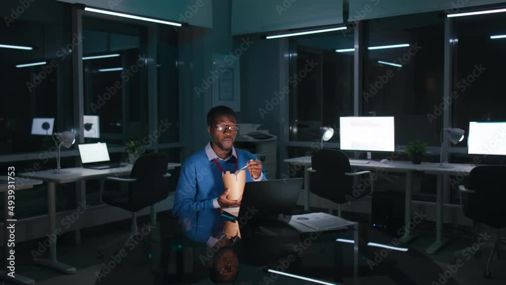 African-American businessman work late in dark office and eat takeaway food African-American businessman work late in dark office and eat takeaway food