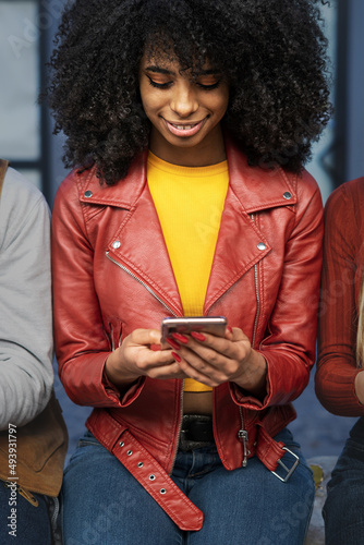 Young African American woman sitting outdoors and using a smartphone - lifestyle concept of younger person addicted to the internet and new technologies photo