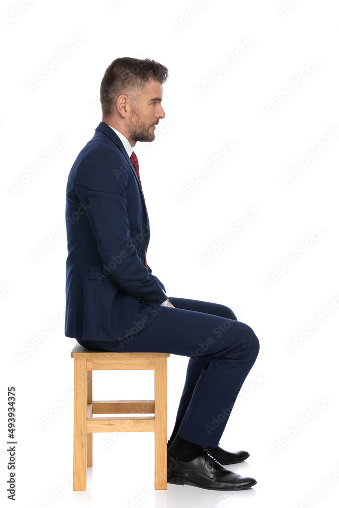 side view of elegant bearded businessman in suit sitting on wooden chair side view of elegant bearded businessman in suit sitting on wooden chair