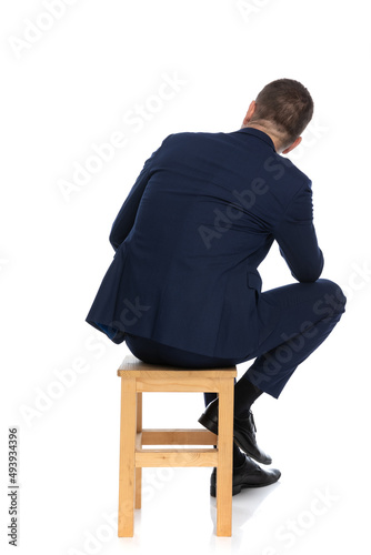 man in elegant suit holding elbow on knee while sitting on wooden chair