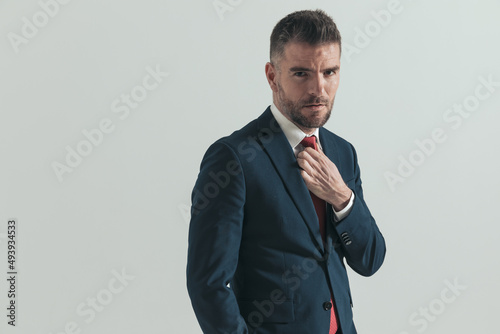 side view of attractive man in suit with hand in pocket fixing red tie