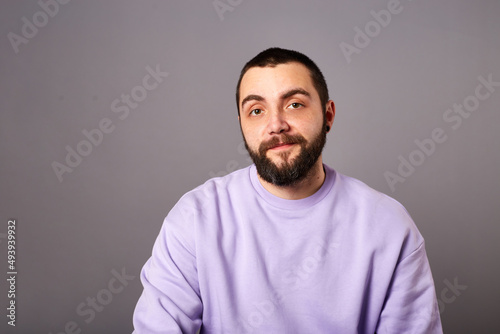 Happy bearded man wears violet sweater on grey background. friendly smile. Copy space