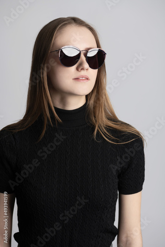 Makeup, beauty and fashion concept. Portrait of beautiful long hair brunette woman with sunglasses. Model wearing black long neck sweater without sleeves in grey studio background with copy space